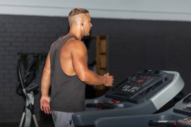 Spor giyimli genç bir adam spor salonunda koşu bandında koşuyor. Koşu bandında koşan yakışıklı bir sporcu. Kapalı alanda atış yapıyor. Koşu bandında spor salonunda koşuyor. Spor yapıyor..