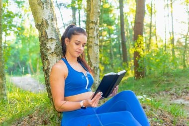 Yaz parkında yeşil çimenler üzerine kitap okuyan genç bir kadın. Kıyafet kitaplarındaki kız. Güneşli bir sabah. Yan manzara..