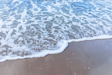 Kumsaldaki yumuşak deniz dalgası, beyaz köpük. Kumsaldaki kumdan kopan dalganın üst görüntüsü. Üst manzara, uzayı kopyala..