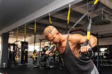 Spor salonunda egzersiz yapan kaslı bir adam, spor salonunda triseps egzersizi yapan. Güçlü çıplak erkek karın kası. Yakışıklı vücut geliştirici. Spor salonunda kapalı alanda çalışıyor..