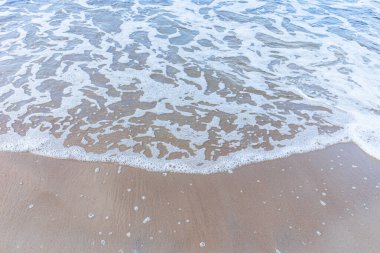 Kumsaldaki yumuşak deniz dalgası, beyaz köpük. Kumsaldaki kumdan kopan dalganın üst görüntüsü. Üst manzara, uzayı kopyala..