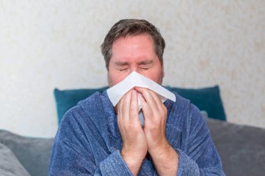 Hasta adam soğuk algınlığı ya da grip, kağıt peçete kullanıyor ve burnu akıyor. Erkek, kalın bornoz giyiyor. Sağlık konsepti. Yakın çekim..