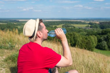 Gezgin dağlarda su içiyor. Sırt çantalı gezgin dağın tepesinde dinleniyor ve güneşli yaz gününde şişe su içiyor..