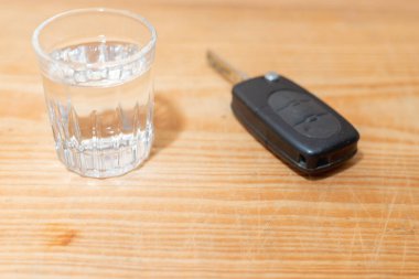 Bir bardak alkollü içecek ve araba anahtarı, ahşap masanın üzerinde. Masada bir bardak votka. Bir bardak votka ve araba anahtarı. Kapalı mekanda çekilmiş..
