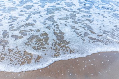 Kumsaldaki yumuşak deniz dalgası, beyaz köpük. Kumsaldaki kumdan kopan dalganın üst görüntüsü. Üst manzara, uzayı kopyala..
