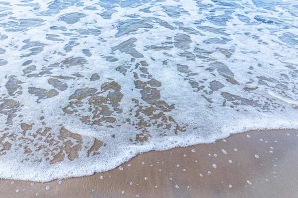 Kumsaldaki yumuşak deniz dalgası, beyaz köpük. Kumsaldaki kumdan kopan dalganın üst görüntüsü. Üst manzara, uzayı kopyala..