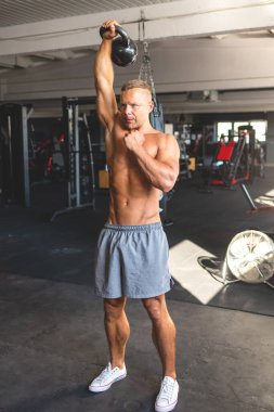 Kettlebell 'le spor yapan formda bir adam. Karanlık arka plandaki adamın fotoğrafı. Kaslı genç adam spor salonunda ağırlık kaldırıyor. Kopya alanı..