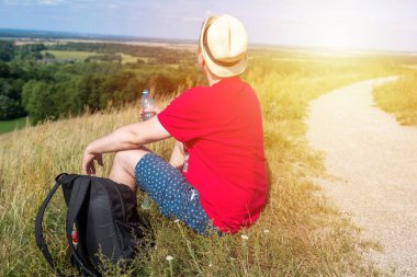Gezgin dağlarda su içiyor. Sırt çantalı gezgin dağın tepesinde dinleniyor ve güneşli yaz gününde şişe su içiyor..