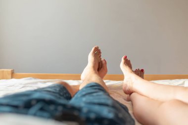 Çiftin ayakları yatağın üstünde. Kadın ve erkek yatakta sevişiyor. Tatil temalı seks. Sevgililer ve Balayı kavramı. Yakın mesafe. Boşluğu kopyala.