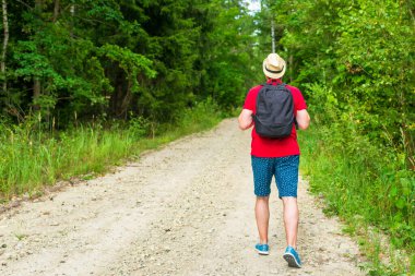 Gezgin genç adam yaz ormanlarında yolda yürüyor. Sırt çantalı genç adam sıcak yaz gününde tek başına ormanı geziyor. Turizm ve aktif yaşam tarzı kavramı..