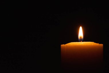 Siyah arkaplanda parlak bir mum yanıyor. Sarı mum alevi. Karanlıktaki mum alevi. Uzayı kopyala..