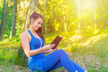 Yaz parkında yeşil çimenler üzerine kitap okuyan genç bir kadın. Kıyafet kitaplarındaki kız. Güneşli bir sabah. Yan manzara..