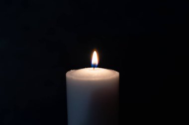 Siyah arkaplanda parlak bir mum yanıyor. Sarı mum alevi. Karanlıktaki mum alevi. Uzayı kopyala..