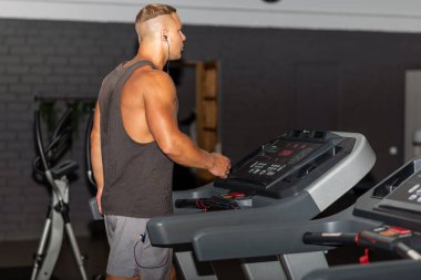 Spor giyimli genç bir adam spor salonunda koşu bandında koşuyor. Koşu bandında koşan yakışıklı bir sporcu. Kapalı alanda atış yapıyor. Koşu bandında spor salonunda koşuyor. Spor yapıyor..