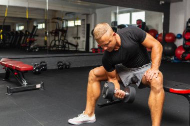 Genç sporcu spor salonunda bisepsi çalışıyor. Spor salonunda ağırlık kaldıran kaslı bir gencin yakın çekimi. Yakın plan..