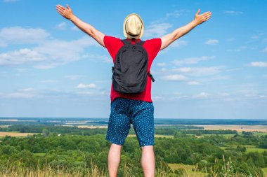Sırt çantalı turist. Sırt çantalı, kollarını açmış gezgin. Mavi gökyüzü beyaz bulutlu yaz manzarasında duruyor.