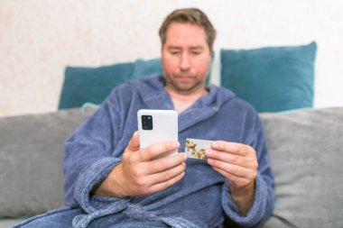 Moda ürünlerini cep telefonuyla kredi kartıyla alan genç bir adam. Online Ödeme. Bankamatik kartı tutan adamın ön portresi ve evden alışveriş için akıllı telefon kullanımı