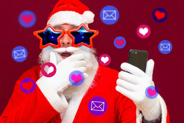 兴奋的圣诞老人得到了社交媒体的关注 圣诞老人在他的手机上使用不同的社交媒体服务 红色工作室背景 — 图库照片