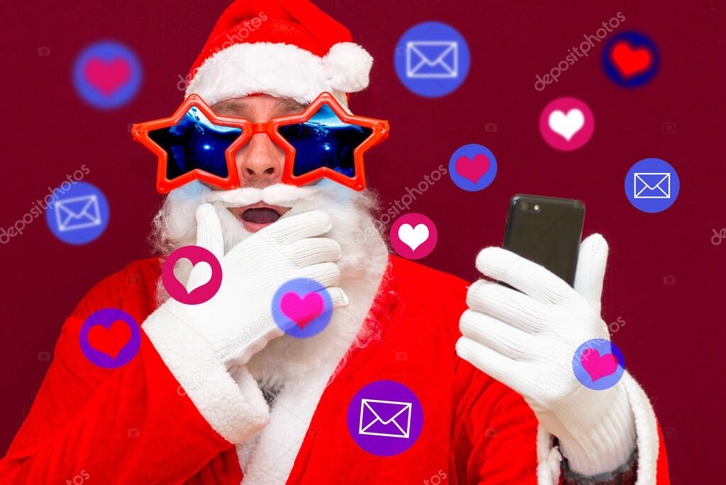 Excited Santa Claus getting attention on social media. Santa Claus using different social media services on his phone.Red studio background.Closeup.