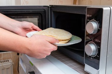 Sağlıksız yemekler, fast food, abur cubur konsepti. İşlenmemiş fast food mikrodalgaya konurken çocuğun eline konan sağlıksız küçük donmuş pizza..