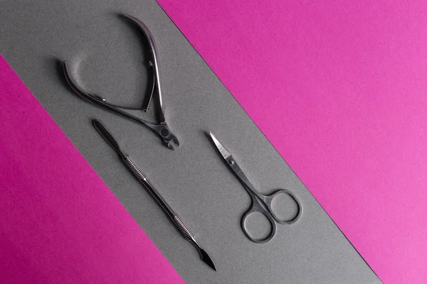 Set of manicure and pedicure tools with space.A classic metal kit of nail scissors and manicure tools on grey and pink background.Nail care objects.