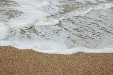 Kumsalda kumlar. Dalgalar kumlara çarpıyor. Beyaz kumlu ve köpüklü dalgalı güzel tropikal plajlar.