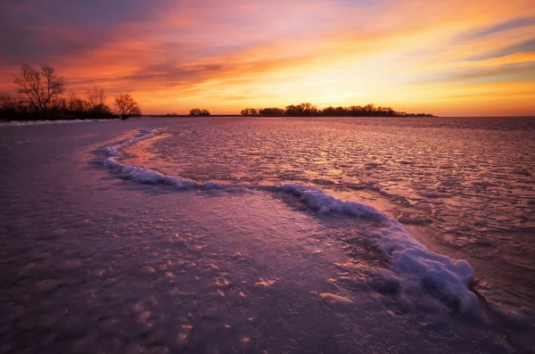 Winterlandschaft mit feurigem Himmel bei Sonnenuntergang und gefrorenem Fluss. — Stockfoto