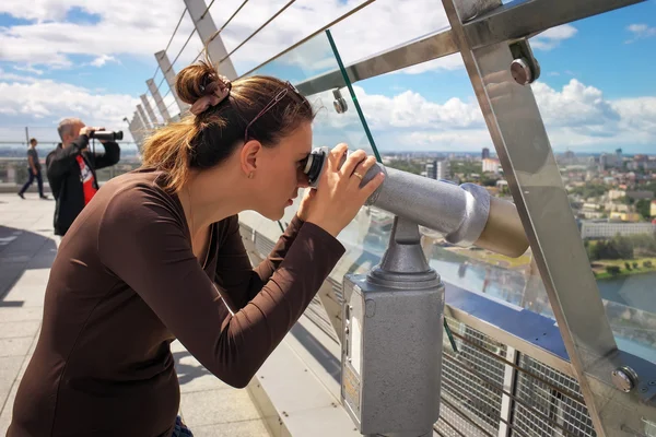 Menina olhando através de um telescópio no telhado de um edifício alto . — Fotografia de Stock