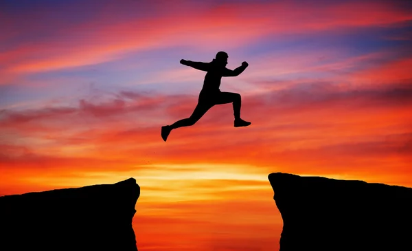 Man jumping across the gap from one rock to cling to the other. — Stock Photo, Image