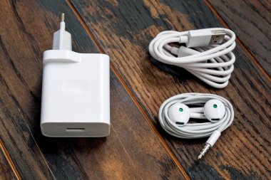 Küçük kulaklıklar ve ahşap arka planda şarj eden cep telefonu kablosu.