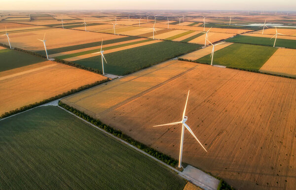 Aerial view of renewable windmills turbines supplying cultivation area with eco power getting energy from wind blowing on vast area of agriculture meadows next to sea. Alternative electricity