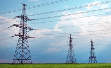 Güneşli bir günde mavi gökyüzünde bulutlar olan düz ve yeşil tarım arazisindeki yüksek voltaj hatları ve elektrik direkleri. Bulutlu ve yağmurlu. Buğday büyüyor.