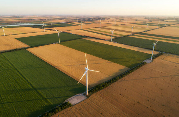 Aerial view of renewable windmills turbines supplying cultivation area with eco power getting energy from wind blowing on vast area of agriculture meadows next to sea. Alternative electricity