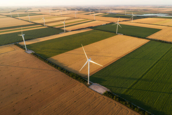 Aerial view of renewable windmills turbines supplying cultivation area with eco power getting energy from wind blowing on vast area of agriculture meadows next to sea. Alternative electricity