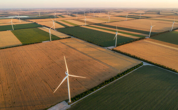 Aerial view of renewable windmills turbines supplying cultivation area with eco power getting energy from wind blowing on vast area of agriculture meadows next to sea. Alternative electricity