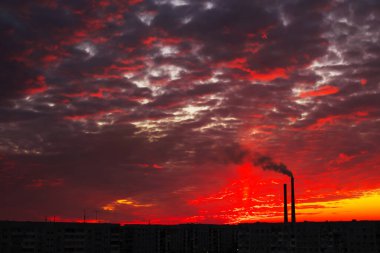 Renkli Sihirli Günbatımı. Gün doğumunda şehir evlerinin çatıları. Kuşlar gökyüzünde uçuyor. Termik santral borusundan siyah duman geliyor..