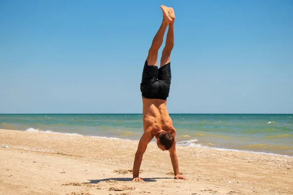 Deniz kenarındaki sahilde fiziksel olarak mükemmel durumda genç ve güçlü bir adam.