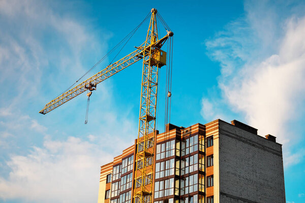 Crane and finished house. Building construction. The top of the building and the sky. 