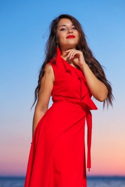 Güneş doğarken ya da batarken sahilde poz veren kırmızı elbiseli güzel esmer kız. 