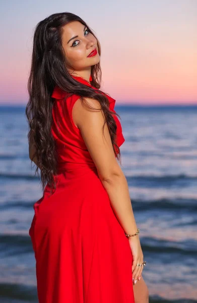 Όμορφη Μελαχρινή Κοπέλα Ένα Κόκκινο Φόρεμα Ποζάρουν Στην Παραλία Κατά — Φωτογραφία Αρχείου