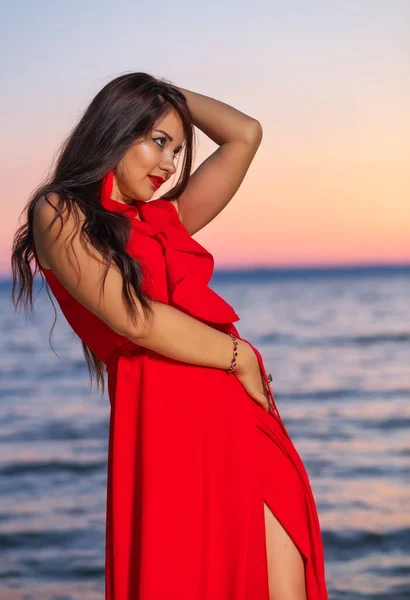 Piękna Brunetka Dziewczyna Czerwonej Sukience Pozowanie Wybrzeżu Podczas Wschodu Lub — Zdjęcie stockowe