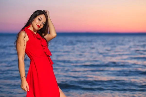 Красива Брюнетка Червоній Сукні Позує Березі Моря Під Час Сходу — стокове фото