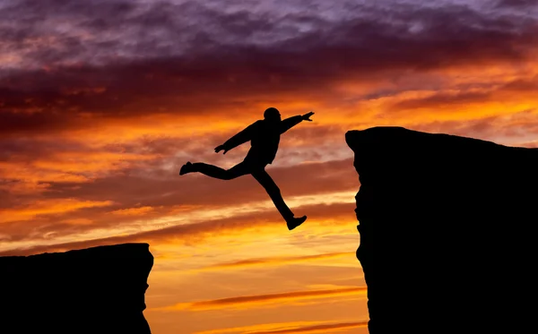 Man jumping across the gap from one rock to cling to the other. — Stock Photo, Image