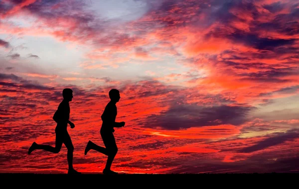 燃えるような夕日を背景に 2 人のランナーのシルエット — ストック写真