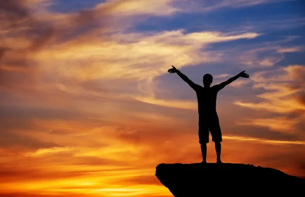 Silhouette of a man on a mountain top on fiery orange background — Stock Photo, Image