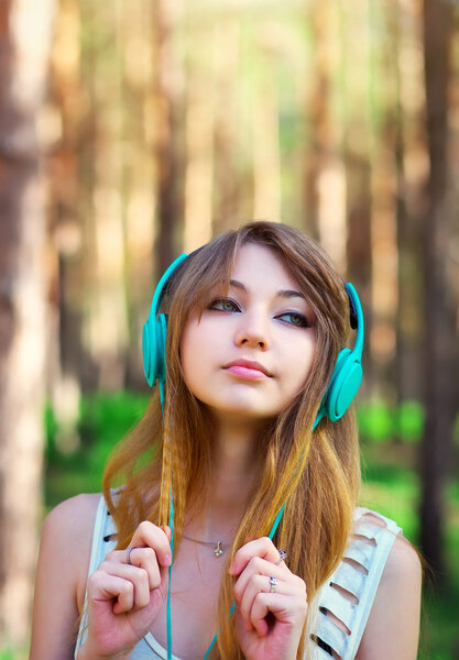 Beautiful girl listening to music with headphones at the par