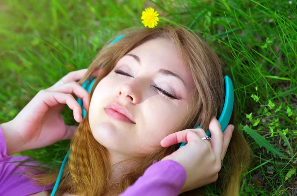 Mooi meisje liggen op het gras en luisteren muziek met headp — Stockfoto