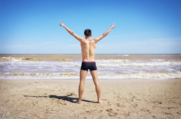 Bakifrån av ung man sprida sina händer på stranden. — Stockfoto