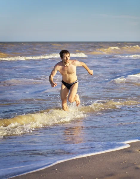 Atlético homem correndo na água na praia — Fotografia de Stock