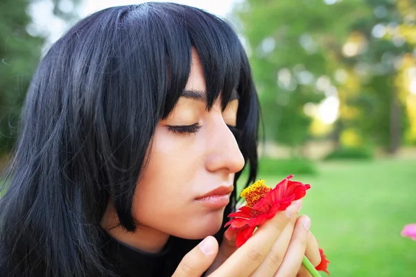Mujer joven oliendo una flor roja al aire libre —  Fotos de Stock